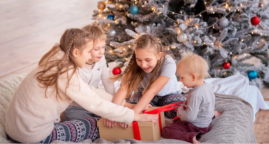 Children opening a gift in the family room near a Christmas tree.